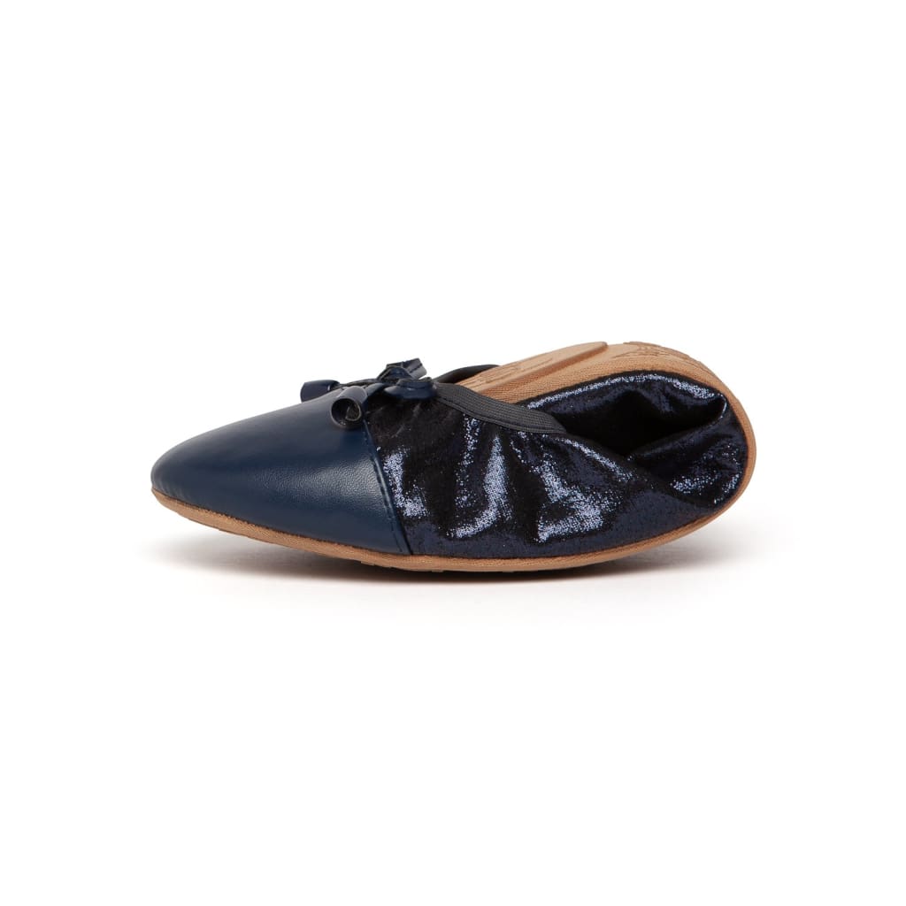 Side view of a foldable navy blue ballet flat with a smooth toe, shimmering heel, and a small bow detail.