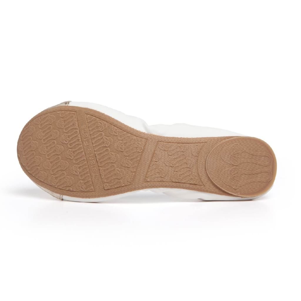 Premium white flat shoe, viewed from below, showing a textured tan rubber sole with brand logo and patterned grip.